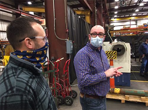 Two men wearing masks are having a discussion in an industrial environment